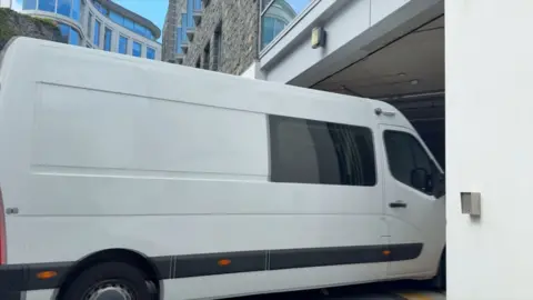 A white van going into the entrance of a building, into the underground car park. 