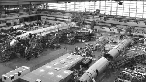 Getty Images Black and white photo of two Concorde prototypes under construction at Filton. One has its fuselage in two parts as its wings are being constructed. There is scaffolding surrounding the planes. 