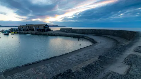 The Cobb stretching out to sea in the early evening. A building is visible at one end.