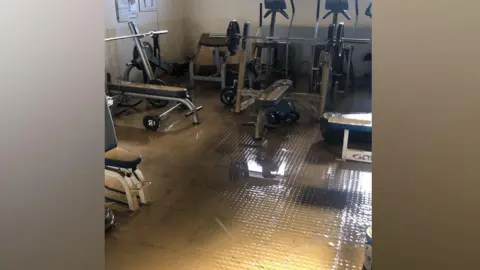 BBOB Rugby Club Gym equipment in a room covered with dirty brown water.