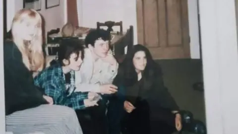 Abbie Eales Teenage girls play a Super Nintendo, sat on a sofa and the floor. Tony McCarroll, wearing a white shirt, looks on.