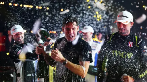 Ian James, Team Principal of Jaguar TCS Racing celebrates winning the team championship on the podium during the London E-Prix, Round 17 of the 2026 FIA Formula E World Championship at ExCel London on 16 August 2026. He has popped a bottle of champagne which is spilling around.