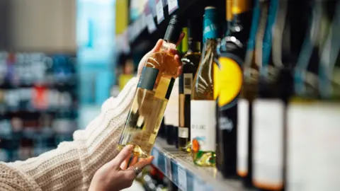 The hands of a woman holding up a bottle of wine in the isle of a shop