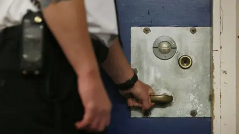Close up of a male prison guard with his hand on the handle of a prison door