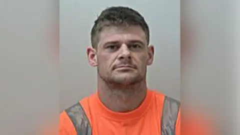 Police handout Police custody image of Adam Garnett with short brown hair and orange t-shirt with a grey strip down the shoulders.
