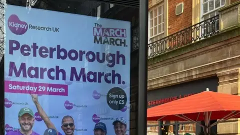 Kidney Research UK The top of a poster advertising the Kidney Research UK Peterborough March March. The words Saturday 29 March are written on a pink banner. The faces of four people can also be seen on the banner. 