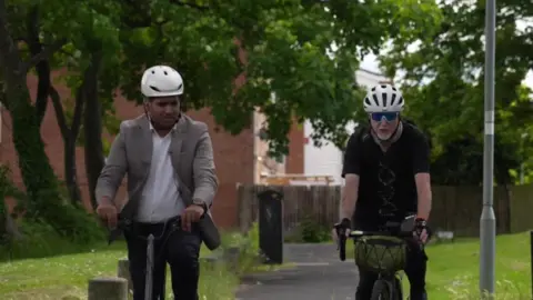 Faisal Islam and Gary Huett riding bikes down a path