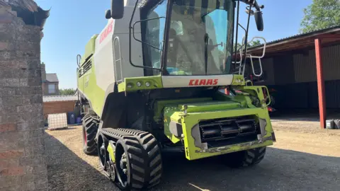 John Devine/BBC A combine harvester which is a big machine that farmers sit in like a truck and cut their crops.