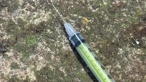 Chelsie Connor Shows a green syringe on the ground