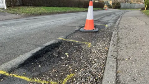 Getty Images A generic image of a pothole damaged road with yellow paint sprayed around the hole and an orange traffic cone warning drivers of the damaged road