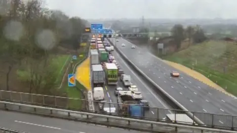 National Highways M1 motorway with queuing traffic on one side.