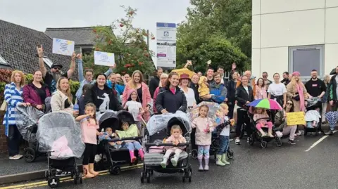 Helen Campbell A large group of protesters including pregnant mums, families all pushing prams in the rain and smiling at the camera 