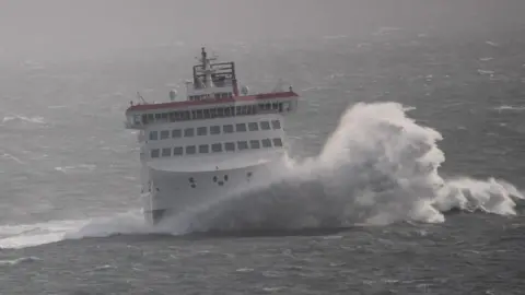 The Manxman ferry, which is white, red and black, hitting a wave in rough seas.