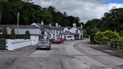 Rob Purvis A quiet village street in southern Scotland with white houses and a pub in the distance and a couple of cars parked up