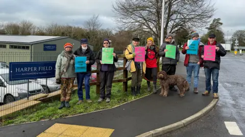 A group of protesters outside an auction house. They are carrying placards speaking against genocide. 