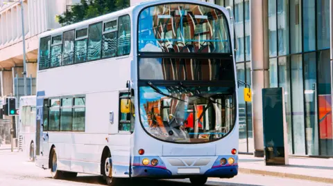 A double decker grey and purple bus in a city centre