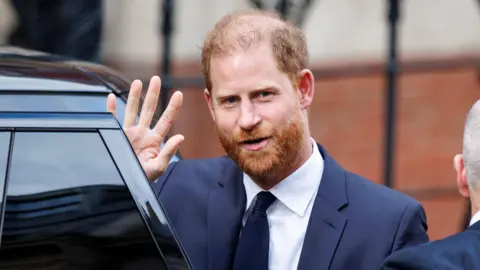 Prince Harry waves as he steps from the door of a black car