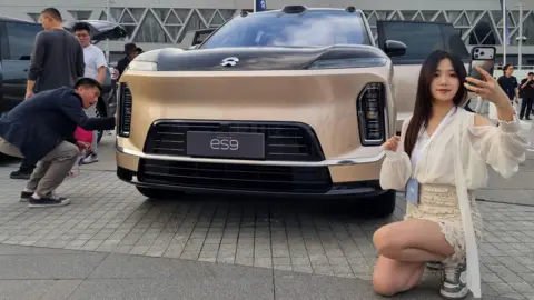  A woman uses her phone near NIO's new flagship electric SUV ES9, displayed ahead of the car's launch event, in Beijing, China 27 May, 2026.