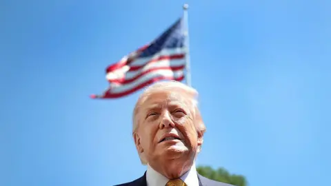 US President Donald Trump speaks in front of the American flag to the press as he departs the White House on May 12, 2026 in Washington, DC. Trump is traveling to China where he is scheduled to meet with Chinese President Xi Jinping for expected talks on the Iran conflict, trade imbalances, regional security, and economic cooperation between the two countries.