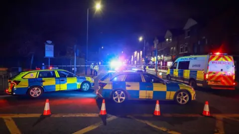 Ashley Stocks Two police cars and a large police van cordon off the street where the man was hit. The scene is in the dark lit up by police lights