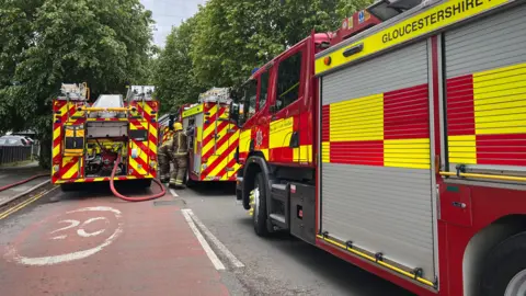 Three fire engines parked on a road in Swindon. Two firefighters are in between two of the fire engines.