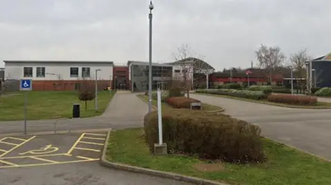 A low-lying school building with a two-storey glazed front and a road leading to the front.