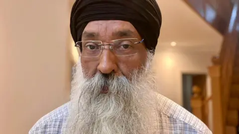 Dabinderjit Singh has a long white beard, glasses and a black turban.