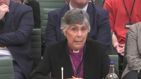 Reverend Dr Guli Francis-Dehqani is talking at a Commons committee in Westminster. She is wearing a purple shirt with a white dog collar. She is wearing glasses and has greying hair.