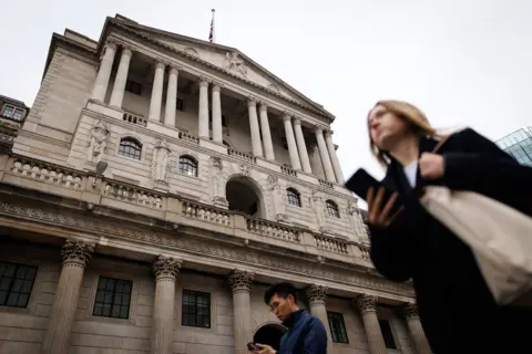 EPA The Bank of England is pictured against a grey sky with people walking in front holding their phones, in Bank, London in December.