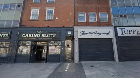 Google An alleyway leading between two shops, a casino slots arcade on the left and cafe with a metal shutter across its front on the right
