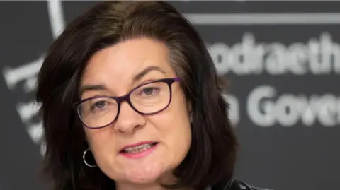 Getty Images Eluned Morgan, wearing glasses and silver hoop earrings, looking seriously at camera