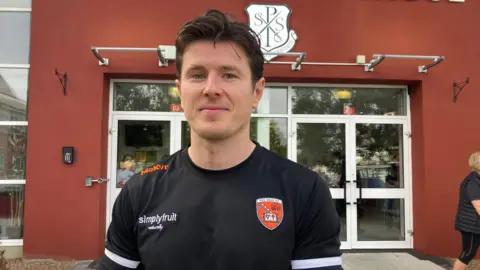 Joe McElroy standing outside the school in an Amragh top smiling at the camera