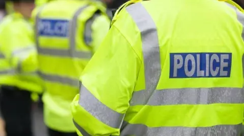 Back of police officers jackets that are bright yellow with police in capital letters in white on a blue background.