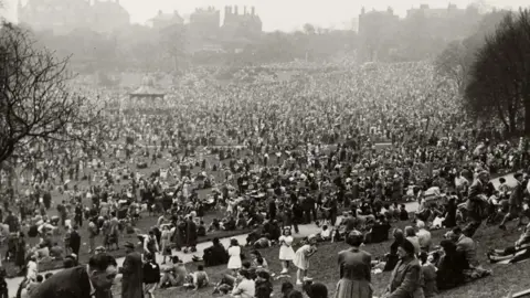 The Harris/Preston City Council A black-and-white photograph, taken from the top of a hill, shows large crowds of people. They are at an outdoor event, with the silhouette of buildings along the skyline in the background.