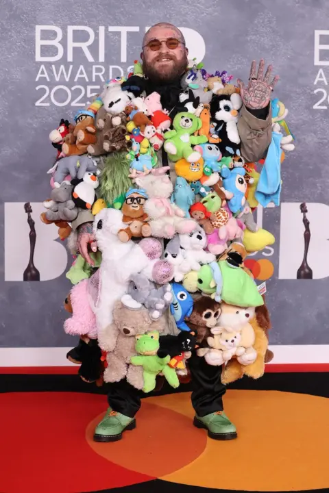 Getty Images El cantante y compositor estadounidense Teddy Swims usa un abrigo hasta el suelo, decorado con cientos de ositos de peluche