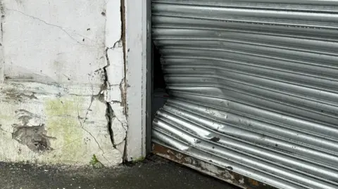 BBC A close-up of a large dent in a metal garage barrier. There is also damage to the wall located on the left.