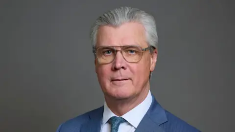 PA Media Malcolm Offord has grey hair and glasses. He has a neutral expression and is posing for a portrait style picture against a grey background 