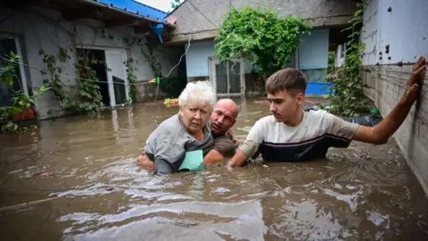 Getty Images Local residents rescue an elderly man (C) from the rising flood waters in the Romanian village of Slobozia Conachi, 14  September 2024. 