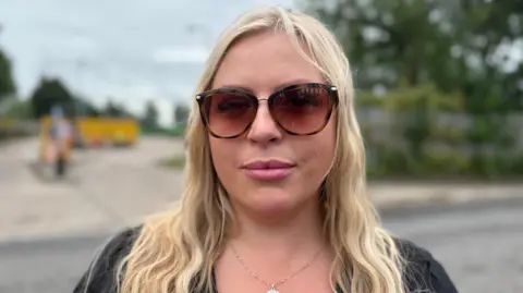 A woman with long blonde hair and wearing brown sunglasses smiles at the camera, while standing in front of the Lincoln tip.
