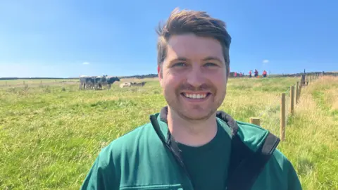 Photograph of Johnny Phillips from United Utilities. He is pictured on the moors above Ramsbottom, with a herd of cows in the background.