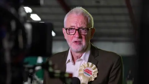 EPA Jeremy Corbyn wearing a white, independent, rosette with his name on