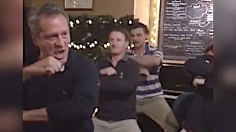 Three men including former New Zealand rugby player Zinzan Brooke are seen doing the haka in a pub.