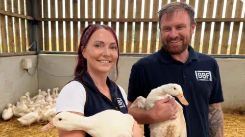 Bernadette Benney and her husband Peter stood holding two ducks and smiling at the camera.