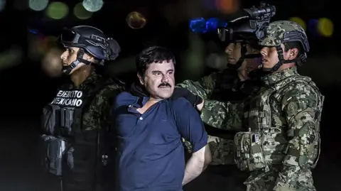 Daniel Cardenas/Anadolu Agency/Getty Images) Joaquín "El Chapo" Guzmán, wearing a blue polo shirt, his hands handcuffed behind his back, is surrounded by Mexican soldiers as he is transported to a maximum security prison in Mexico on 8 January, 2016. 