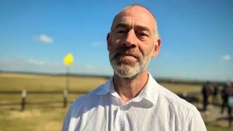 Emma Baugh/BBC Steven Pettican wearing a white shirt and smiling for the camera