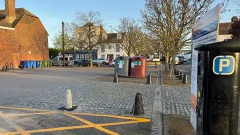 A car park on the Isle of Sheppey. A parking meter is on the right-hand side of the photo and some recycling bins can be seen in the centre.