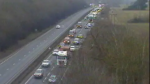 National Highways Traffic queues on the A14 carriageway. Vehicles can be seen backed up closely together as they slowly move along the road.