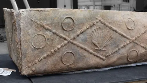 The lead coffin is decorated with a shell and circles embossed on it.