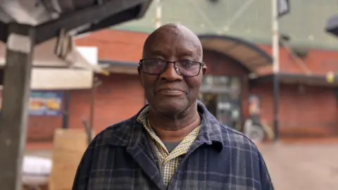 A man with glasses and a tartan shirt stands in front of Leeds Kirkgate Market