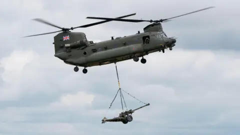 PA Media A helicopter is in the sky demonstrating its capabilities at an air show. It is a military helicopter in grey with the British flag on it.